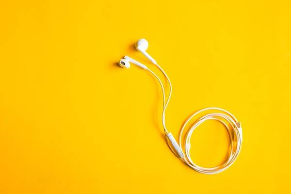 Auf dem Bild liegen weiße In-Ear-Kopfhörer auf gelbem Hintergrund. 