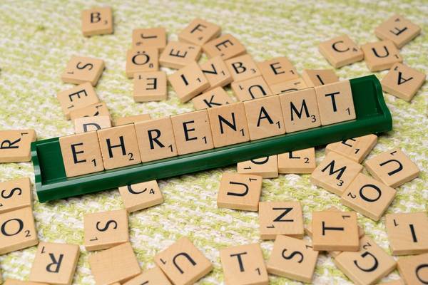 Auf dem Foto ist ein Scrabbel-Spiel zu sehen. Das Wort Ehrenamt ist mit Holzsteinen auf einer einfachen grünen Spielleiste gesetzt. Auf dem Tisch liegen weitere Holzspielsteine mit Buchstaben lose verteilt.